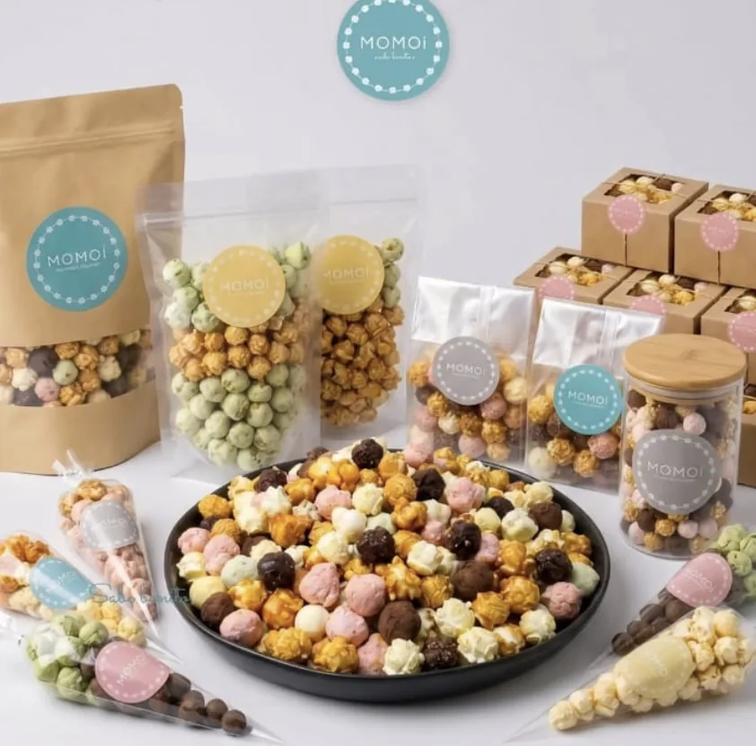 Mesa de evento MOMOi con charola de palomitas de colores, bolsas kraft y transparentes, cajas y frasco con tapa de bambú.