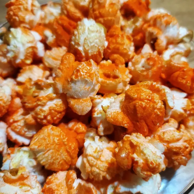 Palomitas con chile naranja servidas en un tazón de vidrio sobre una mesa de madera.